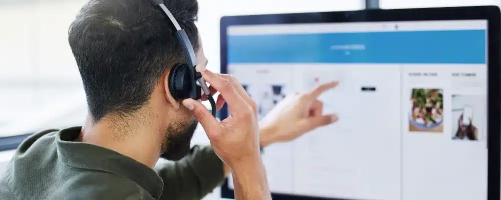 a man talking into his headset & pointing at his computer monitor